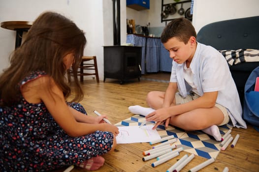 Two kids sit on the floor engaging in drawing activities, creating art with markers amidst a cozy indoor environment, reflecting creativity, childhood, and the joy of crafting.