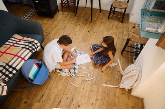 Two children creatively drawing and coloring together on a wooden floor in a cozy room, surrounded by art supplies.