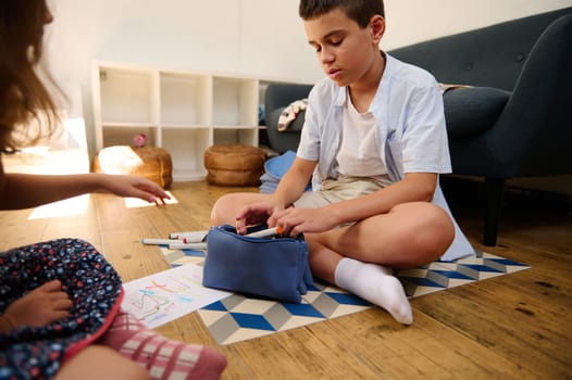 Young boy sitting on floor, drawing with art supplies, creating a cozy educational moment.
