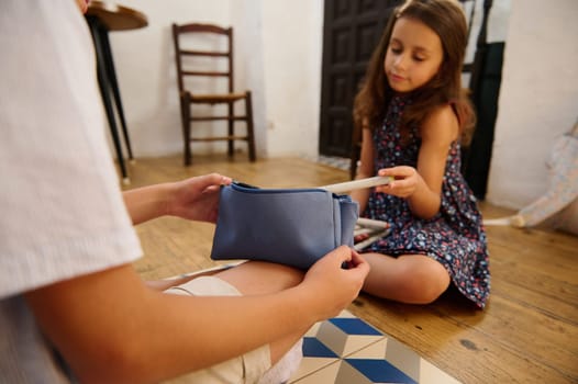 Two children sitting on the floor, exchanging books from a pouch, in a cozy indoor setting.