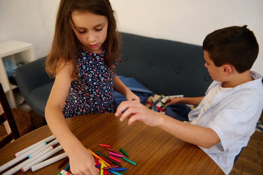 Two children exploring creativity with colorful crafts at a table in a cozy home setting.