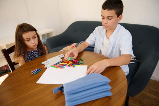 Two kids utilizing colorful markers to create drawings on paper at a table, showcasing creativity.