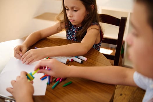Young children sitting at a table focusing on coloring and crafting, showcasing childhood creativity.