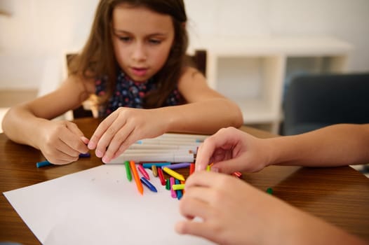 Two kids engaged in a creative activity using colorful crayons on a table indoors.
