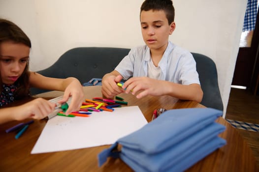 Two children engaging in an arts and crafts activity, using colorful crayons on paper. This indoor moment depicts creativity, focus, and youthful learning and expression at a wooden table.