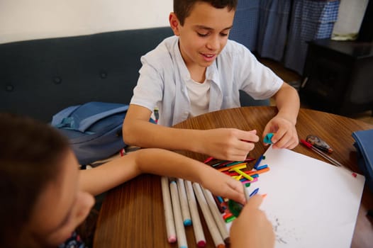 Two children are seated at a table engaging in a drawing activity, surrounded by markers and artwork supplies, fostering creativity and collaboration in a cheerful indoor setting.