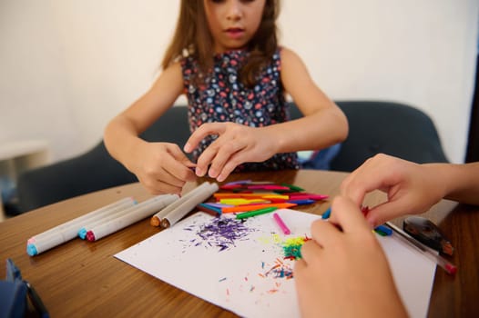 Children engaging in artistic activities with colorful markers and papers, fostering creativity and learning through expressive drawing and coloring on a wooden table in a casual environment.