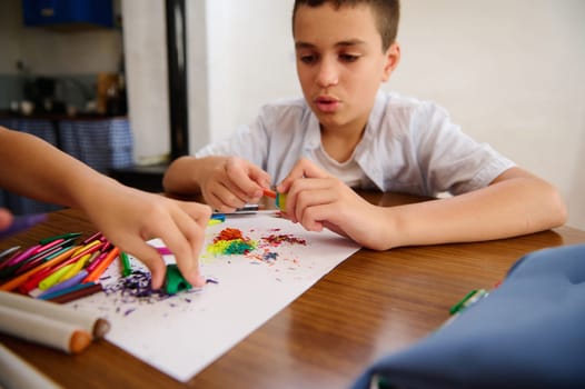Two children explore creativity while making art using vibrant colored pencils and materials on a table, displaying focus and imagination during the crafting process.