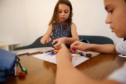 Two children creatively using art supplies on a wooden table, focusing on colorful artistic activities, depicting creativity and collaboration, inspired by learning, teamwork, and expressions of joy.