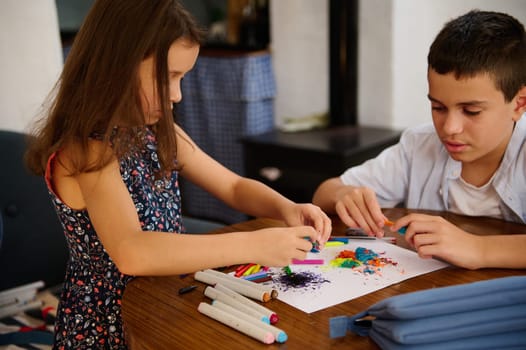 A young boy and girl creating art together using colorful markers and paper at a table.