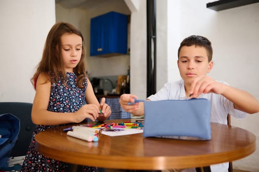 Two children engaged in artistic activities at a table, focusing on coloring tools and items.
