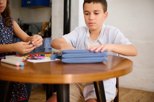 Two children sitting at a wooden table, focusing on arts and crafts, surrounded by colorful stationery in a cozy home setting.