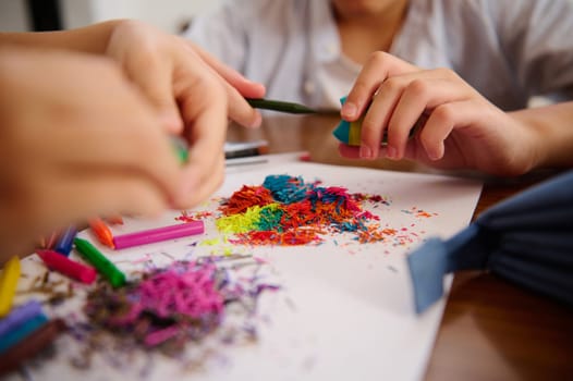 Children creating art with vivid colored shavings and pencils on a table, engaging in artistic fun.