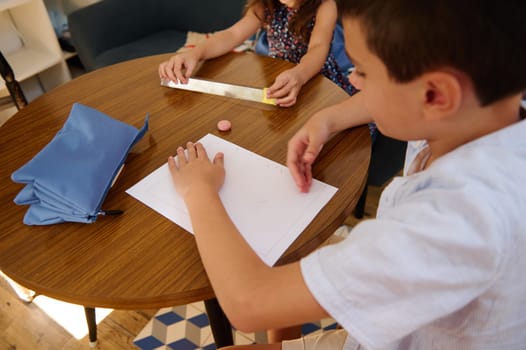 Children sitting at a table working on a creative project with paper and stationery, fostering learning and imagination in a comfortable home environment.