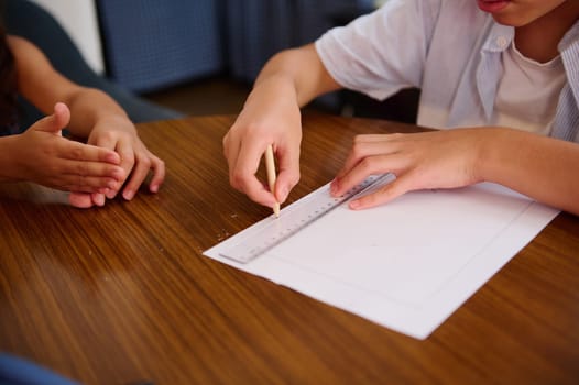 Two individuals drawing lines on paper using a ruler at a wooden table in a collaborative creative activity setting.