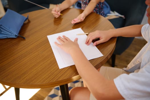 Children sitting at a table, focusing on writing assignments, hands seen with stationery and paper. Ideal for academic, creative learning, and student activities concepts.