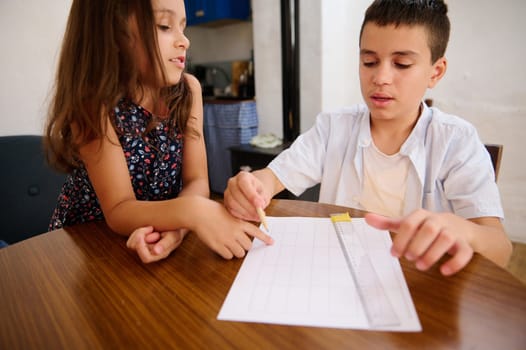 Two children work together on a project, showing teamwork and communication. The image captures learning and cooperation in a warm setting.