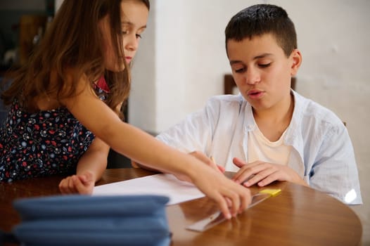 Two children work together on a school project, engaging with paper and a ruler.