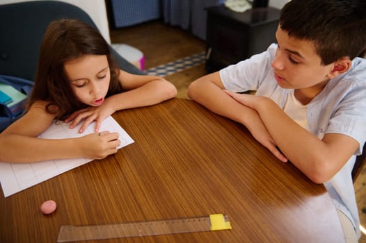 Two children studying together at home around a table, learning and solving problems.