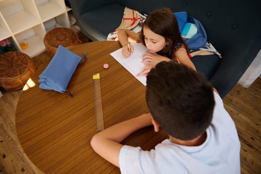 Two children work on their homework at a round wooden table. The scene represents education, collaboration, and learning.