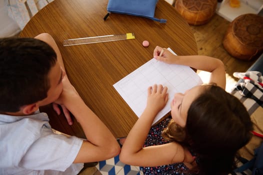 Two children sitting at a table and working on a project or homework. The atmosphere is collaborative with focus and concentration.