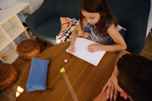 Two children studying and writing at a table indoors, showcasing education and learning in a comfortable and cozy home environment.