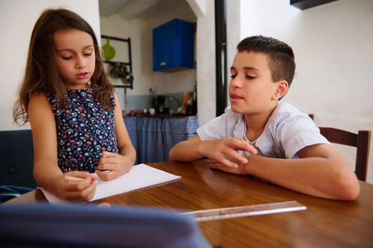 Two children sitting at a table studying together, engaging in homework in a cozy home setting with a focus on learning and concentration.