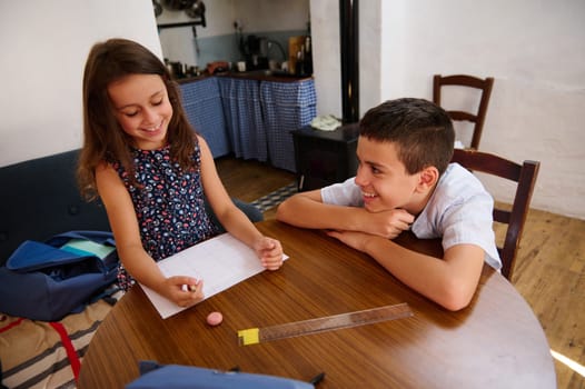Two cheerful children studying at a table, sharing tasks and enjoying their time together in a cozy home environment.