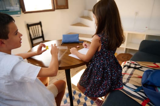 Two children engaging in educational activities at a cozy home table with focused expressions.