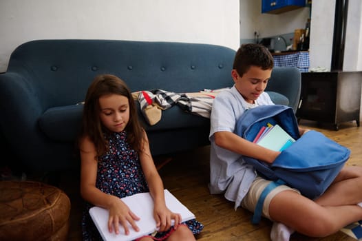 Two children engaged in study activities, sitting on the floor at home, conveying education and concentration.