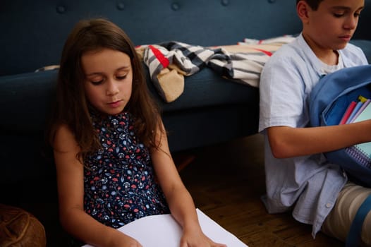 Two children sit together with school materials, concentrating on their homework in a cozy living room setting.