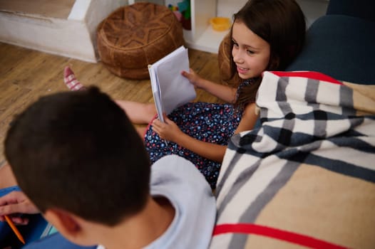Two children enjoy spending time together while reading and chatting on a cozy interior setting.