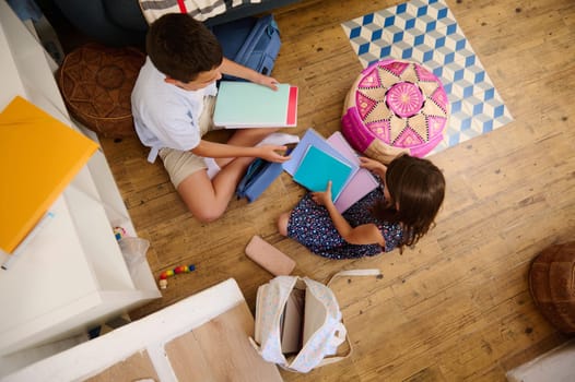 Two children sitting on the floor organizing colorful school supplies, promoting educational preparation, collaboration, and teamwork, set in a cozy and creative home environment.