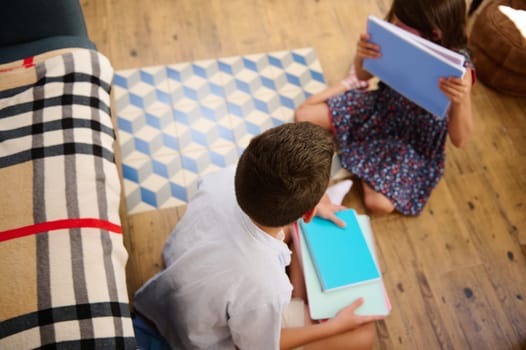 Two children engaged in learning activities, sitting on the wooden floor with notebooks.
