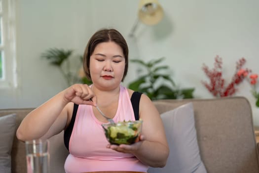 A focused overweight woman attentively eating a fresh salad, emphasizing healthy eating habits and weight loss in a comfortable home setting.