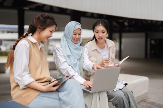 Three diverse female students working together on a laptop in an outdoor campus setting, sharing ideas and collaborating on their project.