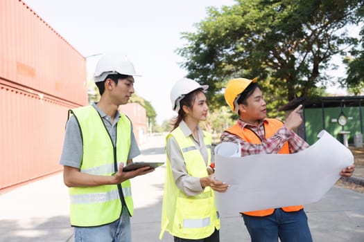 Three construction professionals, including an engineer, a project manager, and a worker, analyzing blueprints and discussing plans at an active construction site.