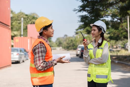 Two construction professionals, a male worker and a female supervisor, communicate about project details while wearing safety vests and hard hats on a construction site.