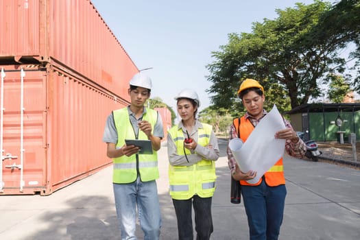 Three construction professionals, including an engineer, a project manager, and a worker, collaborating using blueprints and a tablet at a vibrant construction site.