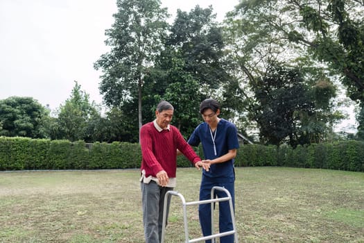 A caring young caregiver assists an elderly man using a walker in a bright garden, promoting mobility and fostering trust in the caregiving relationship.
