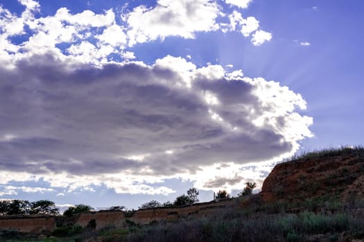view of the sky from the hill, a large cloud above the hill. the sun is breaking through the cloud. a huge space in front of us. the sky is a rich blue color