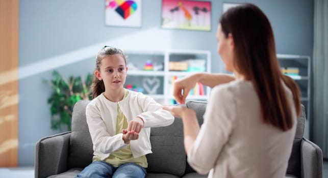 Young girl happily learning sign language from hearing disability teacher.
