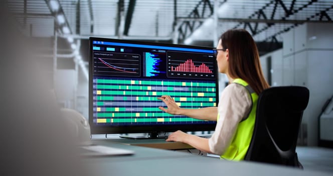 Young engineer using computer to manage production line at factory.   Woman technician connecting energy efficient systems in advanced automated factory.