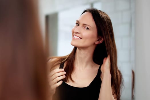 Smiling woman touching her hair, checking for any dandruff. Professional hairstylist doing a keratin treatment on a client's hair. Woman applying facial treatment in front of a mirror