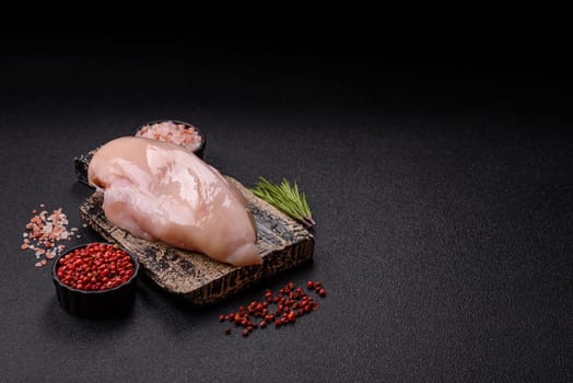 Raw chicken or turkey fillet with salt, spices and herbs on a dark concrete background
