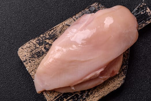 Raw chicken or turkey fillet with salt, spices and herbs on a dark concrete background