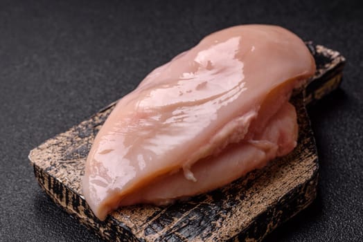 Raw chicken or turkey fillet with salt, spices and herbs on a dark concrete background