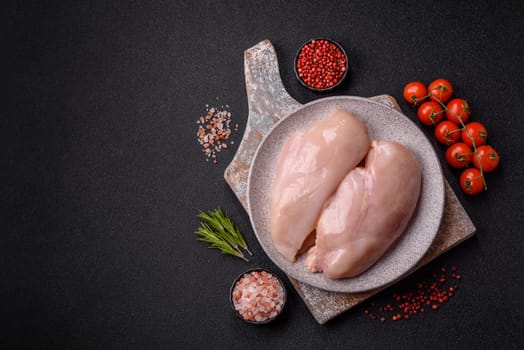 Raw chicken or turkey fillet with salt, spices and herbs on a dark concrete background