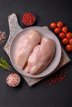Raw chicken or turkey fillet with salt, spices and herbs on a dark concrete background