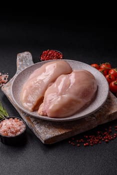 Raw chicken or turkey fillet with salt, spices and herbs on a dark concrete background